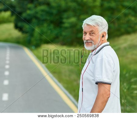 Smiling Old Man Standing On City's Racetrack Looking At Camera.