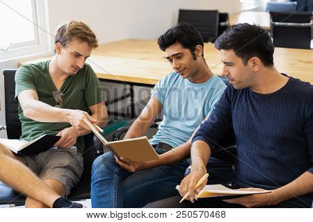 Three Serious Fellow Students Studying, Reading Textbooks And Talking. Young Men Sitting In Armchair