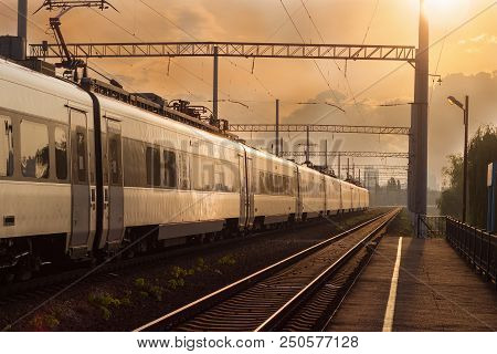 Section Of The Railroad In The City With Moving High-speed Inter-city Train On The Sunset Background