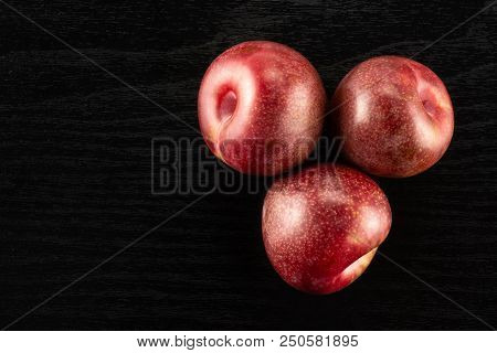 Group Of Three Whole Fresh Pluot Interspecific Plums Variety Flatlay On Black Wood