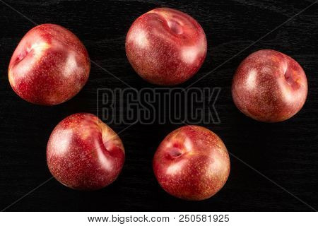 Group Of Five Whole Fresh Pluot Interspecific Plums Variety Flatlay On Black Wood