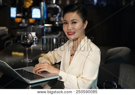 Side View Of Gorgeous Asian Female In Elegant Clothes Sitting At Bar Counter With Glass Of Wine And 
