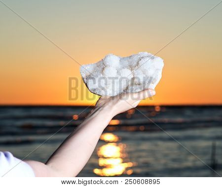Woman Holding Aurora Rainbow Quartz Cluster From India  In Her Hand At Sunrise In Front Of The Lake.