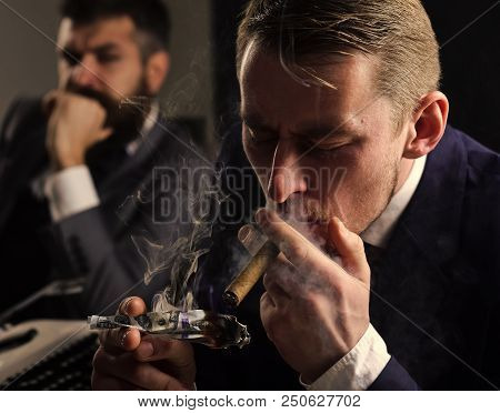 Man Lighting Cigar From Burning Banknote. Businessmen In Suits Sit At Table With Typewriter And Mone