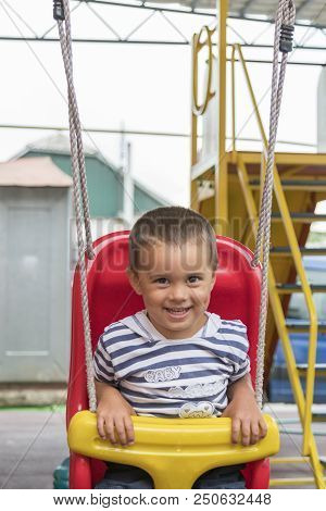 Baby 2 Years Riding On A Swing. Happy Child On The Playground. Ertical Photo.