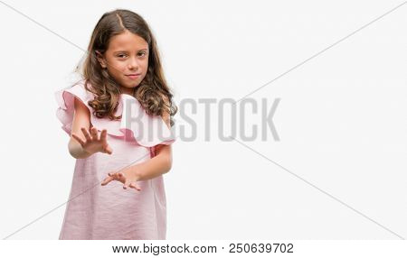 Brunette hispanic girl wearing pink dress disgusted expression, displeased and fearful doing disgust face because aversion reaction. With hands raised. Annoying concept.