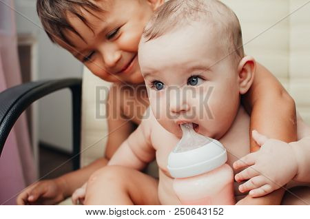 Brother Feeding Little Sister With Milk Or Cereal With A Bottle