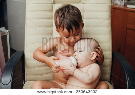 Brother Feeding Little Sister With Milk Or Cereal With A Bottle