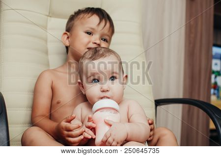 Brother Feeding Little Sister With Milk Or Cereal With A Bottle