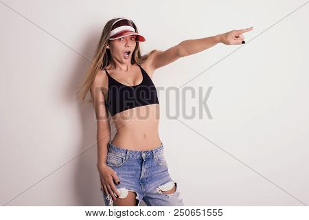 Mischievous Girl In A Red Cap And Jeans Sports Top Amazement Points A Finger To The Side