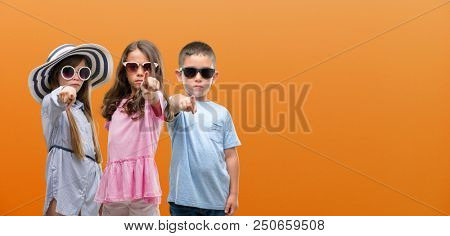 Group of boy and girls kids over orange background pointing with finger to the camera and to you, hand sign, positive and confident gesture from the front