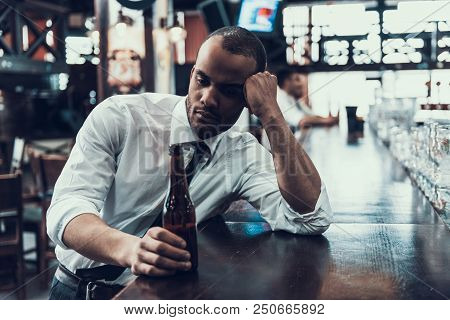 Sad Young Man With Bottle Of Beer Sitting In Bar. Drunken Guy In Modern Pub. Unhealthy Lifestyle. Ad