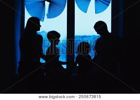 Parents And Kids Sitting Near Window And Having Fun At Home. Silhouette View. Happy Family On The Wi