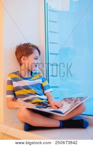 Parents And Kids Sitting Near Window And Having Fun At Kitchen. A Boy With A Book Sits On A Window S