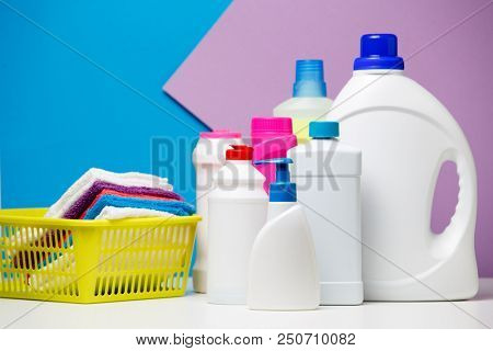 Photo of several bottles of cleaning products and multi-colored towels in basket isolated on violet,blue background