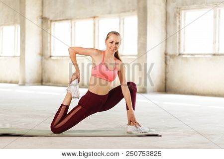 Attractive Young Sportswoman Warming Up Muscles Before Workout In Loft Gym On Promotional Background