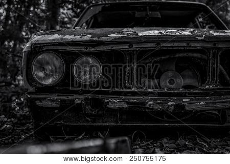 Old Wrecked Car In Black And White Scene. Abandoned Rusty Car In The Forest. Closeup Front View Of D