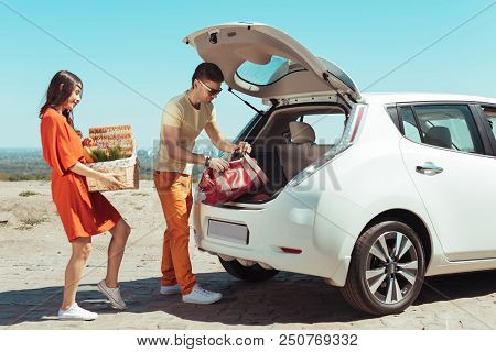 Going To Picnic. Modern Couple Taking Their Things Out Of White Fancy Car While Going To Picnic