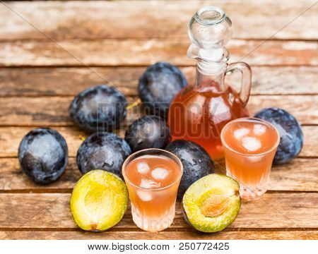 Close Up Plum Liqueur Or Slivovitz, Plum Rakia With Fresh And Tasty Plums In Wooden Bowl On Wooden B