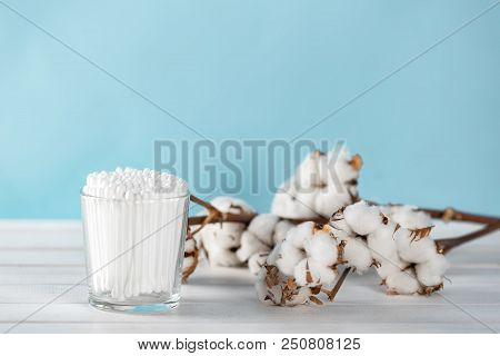 Cotton Swabs In Clear Glass Jar In Bathroom Setting With A Cotton Flowers On Pastel Blue Background.