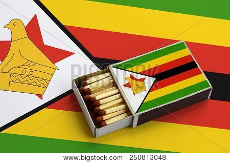 Zimbabwe Flag  Is Shown In An Open Matchbox, Which Is Filled With Matches And Lies On A Large Flag.