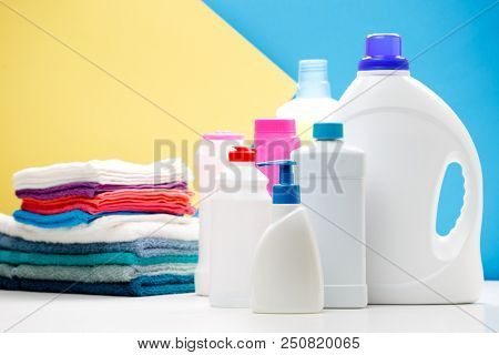 Photo of several bottles of cleaning products and colored towels on table isolated on blue, yellow background