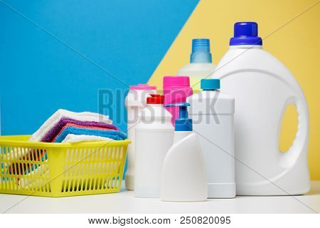 Photo of several bottles of cleaning products and multi-colored towels in basket isolated on yellow,blue background
