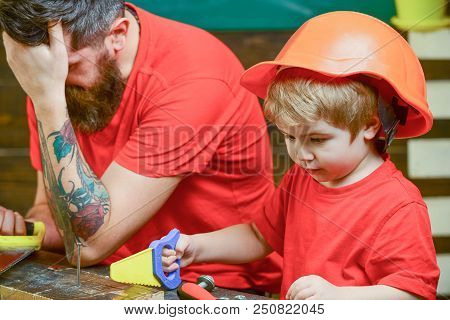 Educational Games Concept. Boy, Child Busy In Protective Helmet Learning To Use Handsaw With Dad. Fa