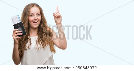 Young blonde woman holding passport of canada and boarding pass surprised with an idea or question pointing finger with happy face, number one