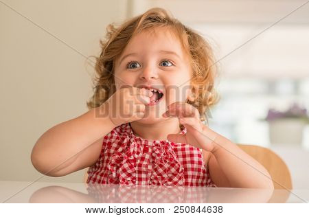 Beautiful blonde child with blue eyes smiling and eating candy at home.