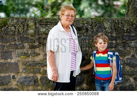 Grandmother Taking Child, Kid Boy To School. Pupil Of Primary School Go Study. Senior Woman Holding 