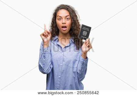 Young hispanic woman holding passport of Italy surprised with an idea or question pointing finger with happy face, number one