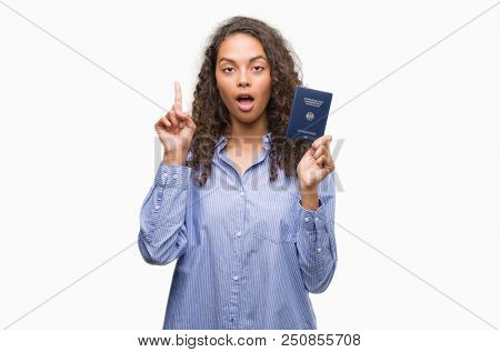 Young hispanic woman holding passport of Germany surprised with an idea or question pointing finger with happy face, number one