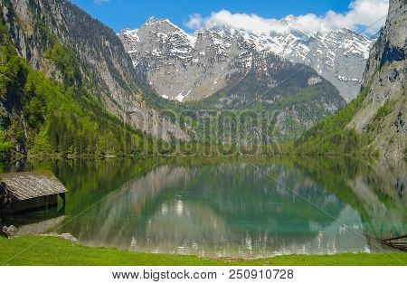 A Small House On The Shore Of The Emerald Lake Mittersee, Surrounded By Alpine Peaks.