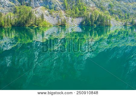 The Harsh Rocks And Gentle Greenery Are Reflected In The Mountain Lake Obersee.