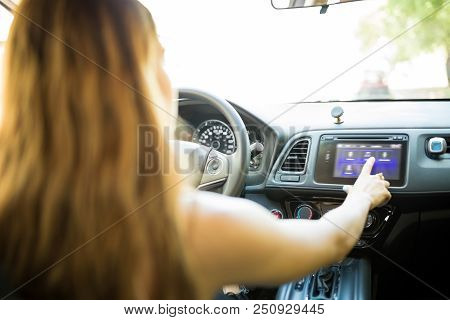 Rear View Of Young Woman Using Touchscreen Infotainment While Driving Car