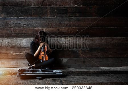 The Lady Is Sitting On Grunge Surface Cement Floor,hold Violin And Bow In Her Arms,turn Face Down To