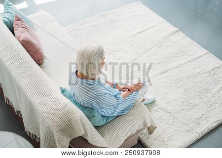 High Angle View Of Senior Woman With Remote Control Watching Tv On Sofa At Home