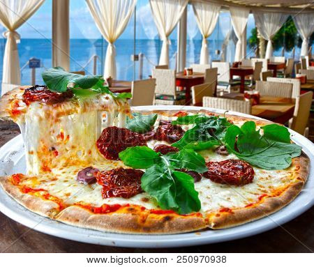 Pizza with dried tomatoes, rucula and mozzarella in pizzeria overlooking the sea