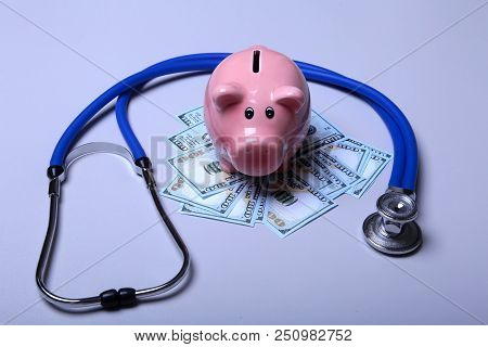 Piggy Bank With Dollar Notes And Stethoscope On A Wooden Desk.