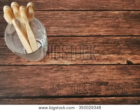 A Family Set Of Four Wooden Toothbrushes In A Glass On Wooden Background With Copy Space