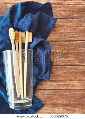 A Family Set Of Four Wooden Toothbrushes In A Glass On Blue Fabric With Copy Space