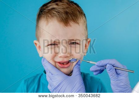 Small Patient Does Not Want To Open The Dentists Mouth On Blue Background. Dantist Treats Teeth. Clo