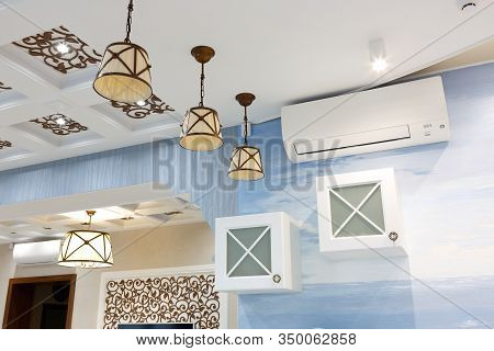 The interior of the kitchen. Blue walls, white ceiling. There are three chandeliers on the ceiling, the air conditioning on the wall. Cupboards with shelves. A florid pattern. Interior design.