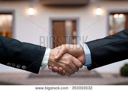 Buying A House Concept. Two People Handshake In Front Of The New Hosue With Copy Space