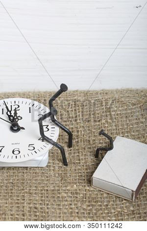 Figurines Of Man Made From Carpentry Nails. They Are Sitting On The Watch Dial, Next To Each Other.
