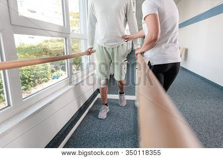 Therapist helping young man learning to walk again in rehabilitation on the bars