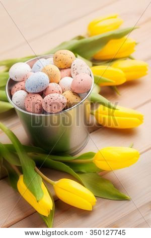 Pastel Easter egg candies with yellow tulips. Easter holiday concept.