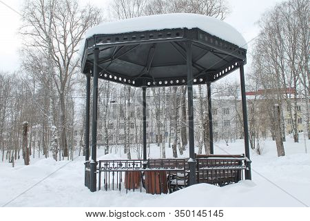 Metal Open Gazebo With Benches In Park, Covered With Snow On Cloudy Day. Concept Of Improvement And 