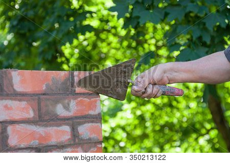 Masonry Works, Male Hand Working With A Trowel, Repairing A Chimney From Red Bricks On A Roof Of Cou